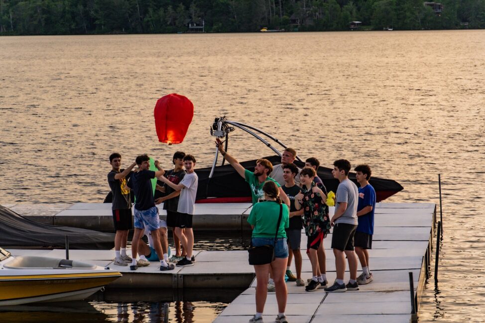 campers on the lake at dusk sending lanterns into the sky